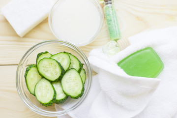 Obraz na płótnie Canvas Cucumber home spa and hair care concept. Sliced cucumber, bottles of oil, soap, jar of mask, bathroom towel. White board background