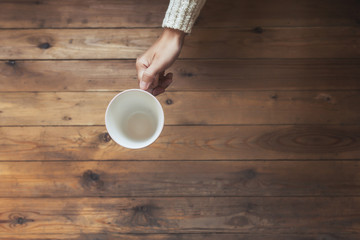 A girl hands with an empty cup for coffee on the wooden table background. Winter concept