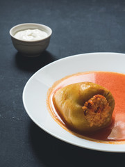 Stuffed pepper in a white plate with sour cream on a black background