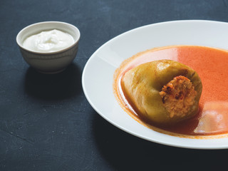 Stuffed pepper in a white plate with sour cream on a black background