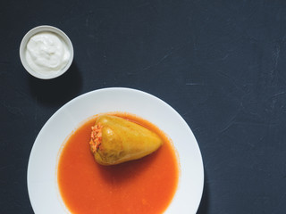 Stuffed pepper in a white plate with sour cream on a black background. Flat lay, top view, copy space
