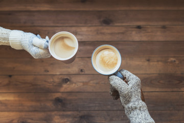Male's and female's hands in the winter knitted mittens with an cup of coffee on the wooden table background. Winter concept