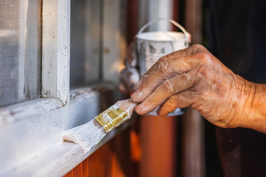 Senior man painting wooden windows using paintbrush. Repairing exterior of old house. 