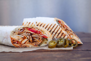 Shawarma sandwich gyro- fresh roll of thin lavash (pita bread) filled with grilled meat, mushrooms, cheese, cabbage, carrots, sauce, green. Traditional Eastern snack. On a wooden background