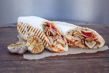 Shawarma sandwich gyro- fresh roll of thin lavash (pita bread) filled with grilled meat, mushrooms, cheese, cabbage, carrots, sauce, green. Traditional Eastern snack. On a wooden background
