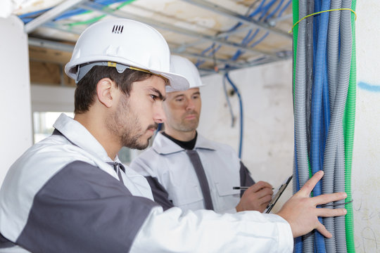 professional electrician with student on construction site
