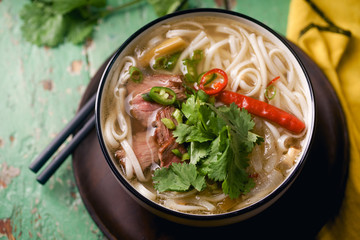 Vietnamese traditional soup Pho Bo with beef and fresh coriander on rustic wooden table