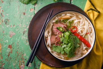 Vietnamese traditional soup Pho Bo with beef and fresh coriander on rustic wooden table