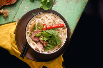 Vietnamese traditional soup Pho Bo with beef and fresh coriander on rustic wooden table