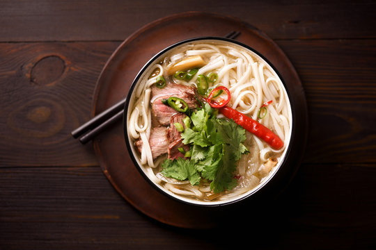 Vietnamese traditional soup Pho Bo with beef and fresh coriander on dark wooden background