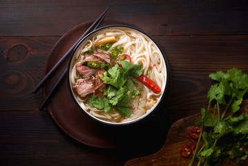 Vietnamese traditional soup Pho Bo with beef and fresh coriander on dark wooden background