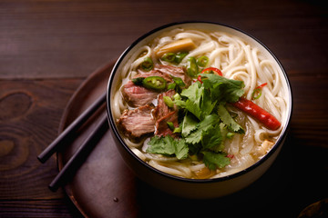Vietnamese traditional soup Pho Bo with beef and fresh coriander on dark wooden background