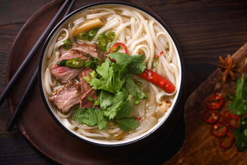 Vietnamese traditional soup Pho Bo with beef and fresh coriander on dark wooden background
