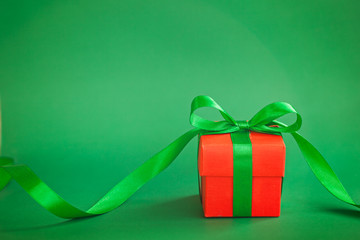 One red christmas gift box with green ribbon on green background