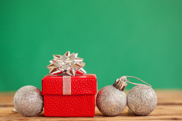 Red christmas gift box with green ribbon and three xmas balls on green background