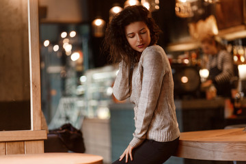 beautiful brunette in a gray knitted sweater poding on camera in a cozy warm cafe in a cold autumn