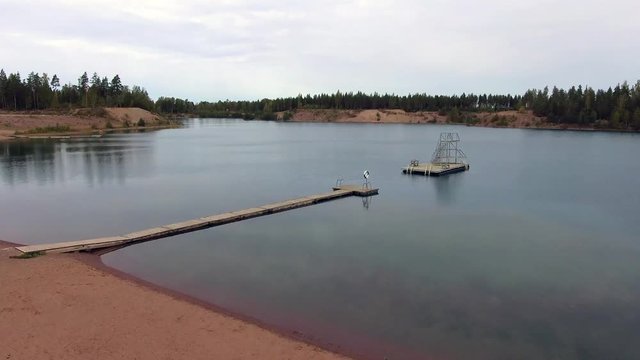 Aerial view of sandy beach, wooden pier and diving tower on small lake.