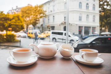 two cups with tea and white kettle in cafe table with big glass window