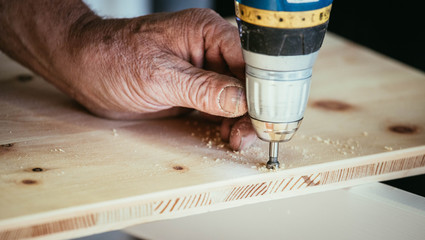 Handwerker bohrt Loch in Holzplatte, Hände und Bohrmaschine, Heimwerker