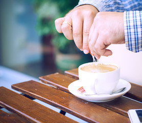 Young man hands holding sugar bag and sweetens coffee in a cafe.
