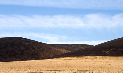 Fototapeta na wymiar California drought parched brown fields with fire scorched hills in the background. Blue cloudy sky.