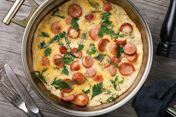 Scrambled eggs with sausage and greens in frying pan, top view, closeup