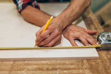 craftsman measuring with ruler and pencil on a wood board