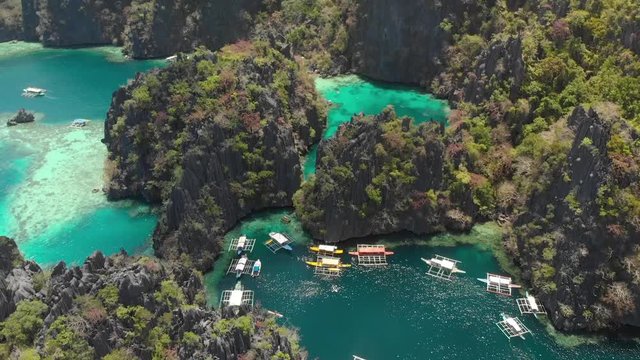 Aerial tilt drone shot of turquoise lagoons, limestone cliffs and Paraw boats, on a sunny day in Coron island, Philippines, Asia