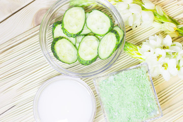 Cucumber home spa and hair care concept. Sliced cucumber, bottles of oil, sea salt, bathroom towel. Straw light background