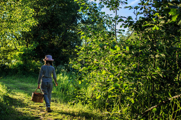 Young girl walking on a path through green woods carrying a birchbark basket