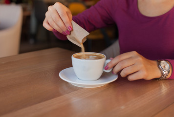 Young woman adding sugar in coffee	