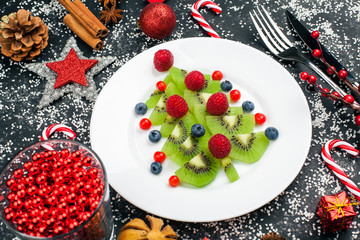 Kiwi christmas tree with raspberry, blueberry and cowberry on table with decoration