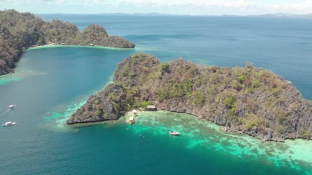 Aerial tilt drone shot over turquoise lagoons, and towards limestone cliffs and Paraw boats, at a paradise isle, on a sunny day, at Coron island, Philippines, Asia