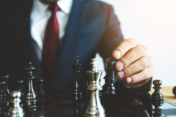 Retro style image of a businessman with clasped hands planning strategy with chess figures on an old wooden table.