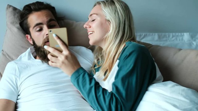 Couple using mobile phone on bed at home 4k