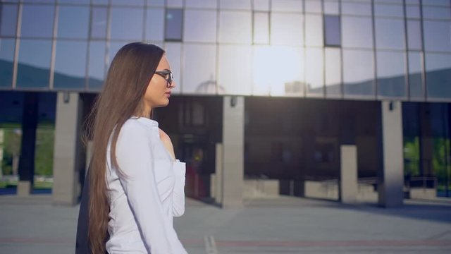 Side view of young successful businesswoman or femele student, woman wearing modern suit white shirt and walking in the city outdoors, flare light, sunshine, slow motion. Business, startup, education
