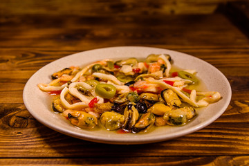 Ceramic plate with different sea food and olives on wooden table
