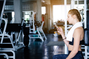 Young sporty girl  resting after an intense workout in gym with smartphone listening to music