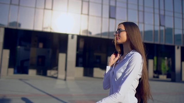 Side view of young successful businesswoman or femele student, woman wearing modern suit white shirt and walking in the city outdoors, flare light, sunshine, slow motion. Business, startup, education