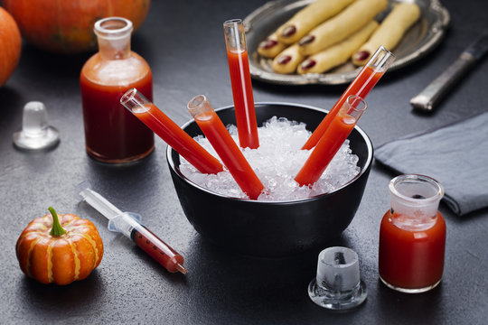 Bloody Mary cocktail in glass tubes with Witch's fingers cookies for Halloween party celebration. Black stone background
