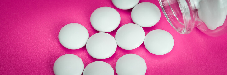 White pills are scattered from a glass bottle on a pink background. Vignetting