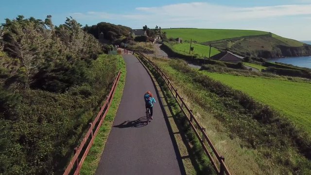 Redhead Woman Cycling Along The Ocean Coast. Waterford Greenway In Ireland 