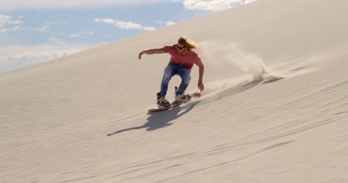 Man sand boarding on the slope in desert 4k