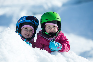 Identical twins are having fun in snow. Kids with safety helmet. Winter sport for family. Little kids outside, swiss Alps, mountains, healthy lifestyle, cheerful family, smiling cute girls
