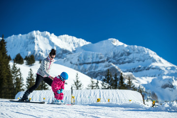 Mother and little child skiing in Alps mountains. Active mom and toddler kid with safety helmet, goggles and poles. Ski lesson for young children. Winter sport for family. Little skier, swiss Alps
