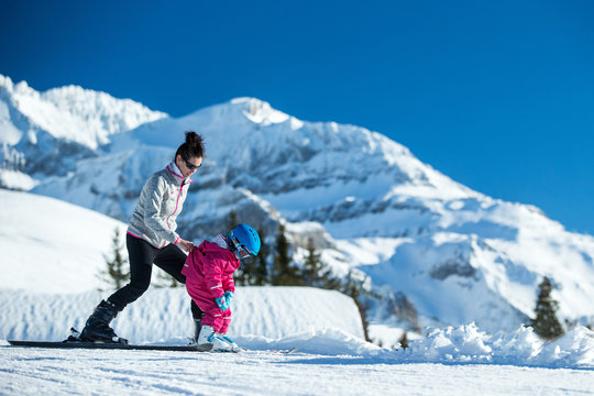 Mother and little child skiing in Alps mountains. Active mom and toddler kid with safety helmet, goggles and poles. Ski lesson for young children. Winter sport for family. Little skier, swiss Alps