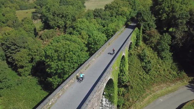 Aerial View Of Man And Woman Cycling Against Each Other On The Bridge In Rural Green Nature Landscape. Waterford Greenway, Ireland.