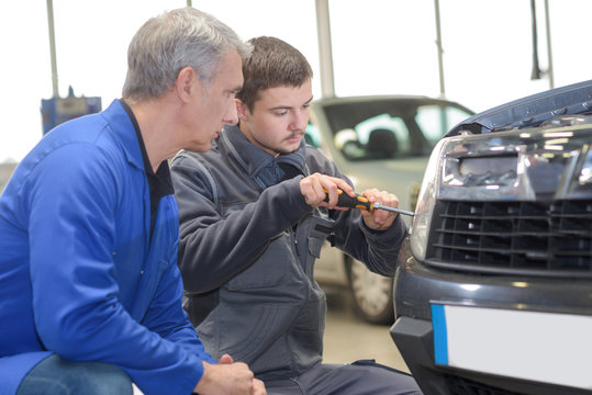 student and teacher mechanics changing car headlight in a workshop
