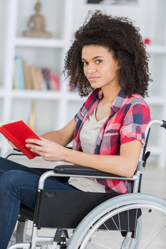 young worried woman in wheelchair holding book