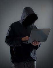 Hacker with hidden face in a hoodie using a laptop